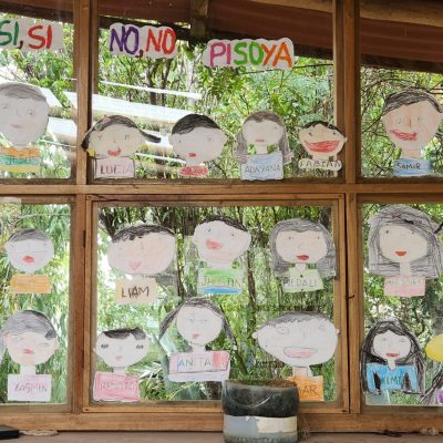 A window with wooden frame covered with cut-outs of children's self-portraits on paper.