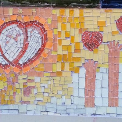 mosaic wall with white hearts outlined in red and hands reaching up to small red hearts