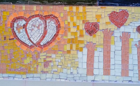 mosaic wall with white hearts outlined in red and hands reaching up to small red hearts