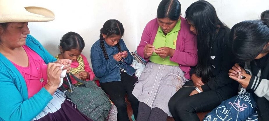 women and children sit side by side knitting