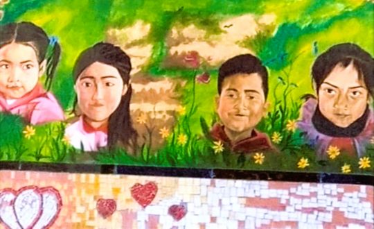 painted mural shows portraits of four children against a background of grass and dirt and below them a mosaic of hearts and hands